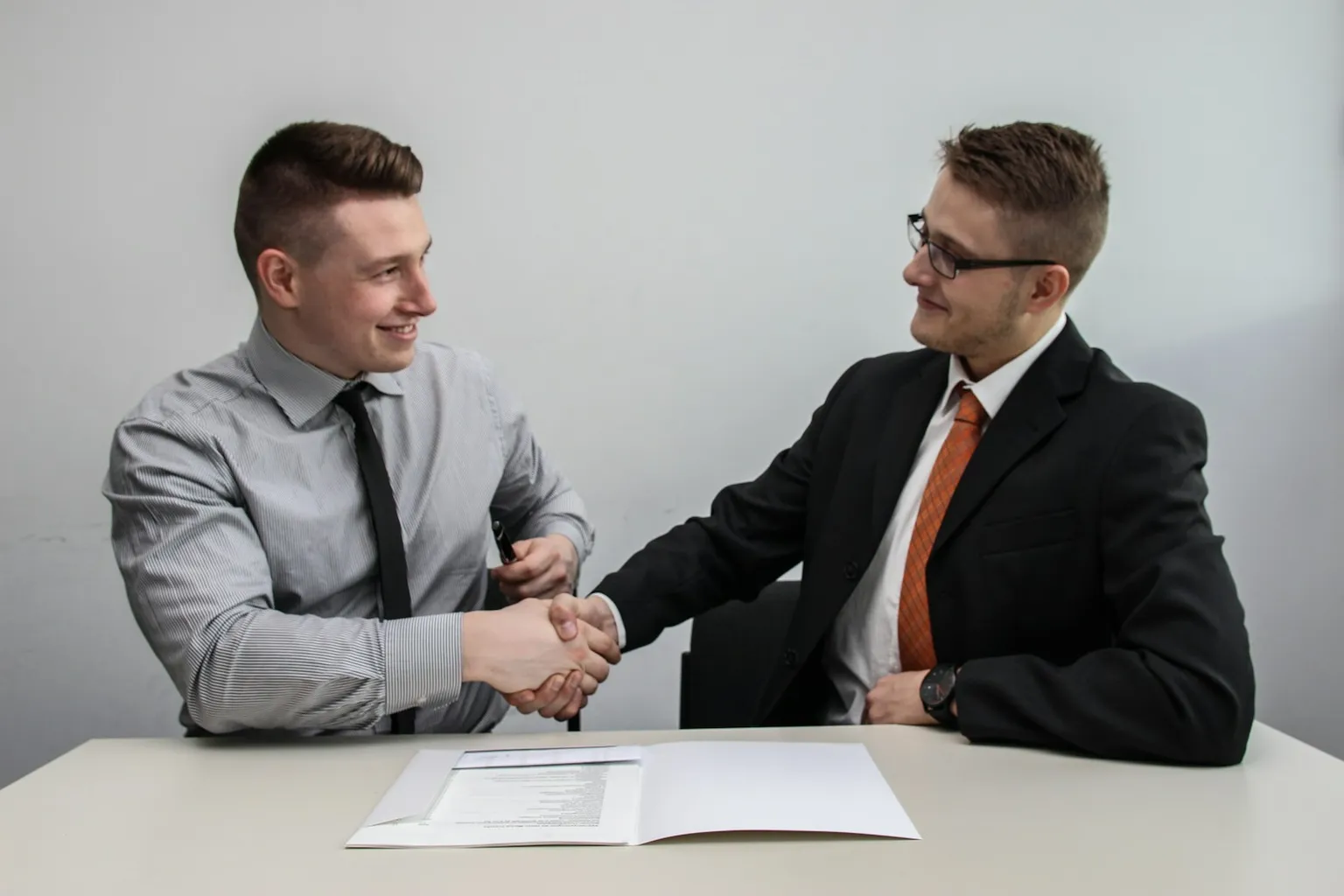 Two men shaking hands over a folder of documents